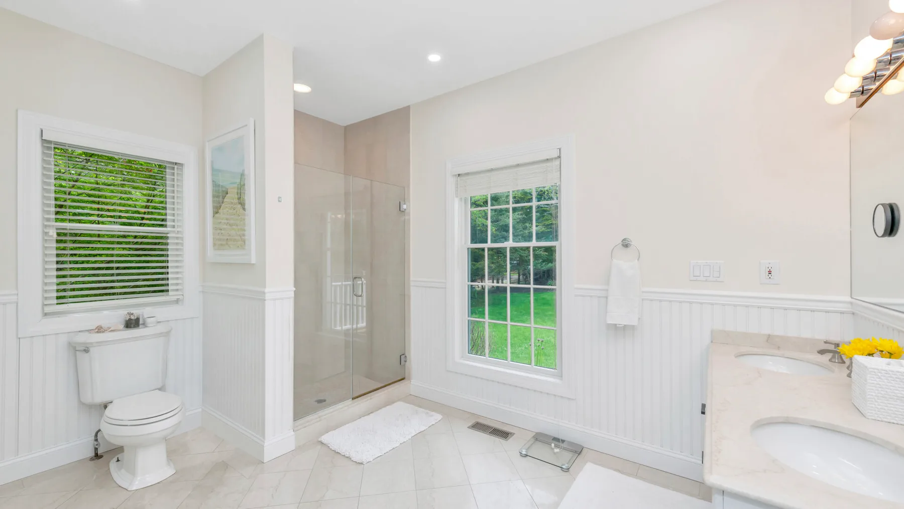Un baño luminoso con ducha de vidrio, inodoro y ventanas con vista a la vegetación.