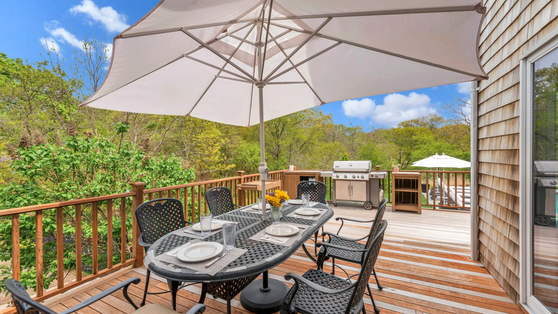 Comedor en una terraza exterior con una sombrilla grande sobre una mesa y asientos.