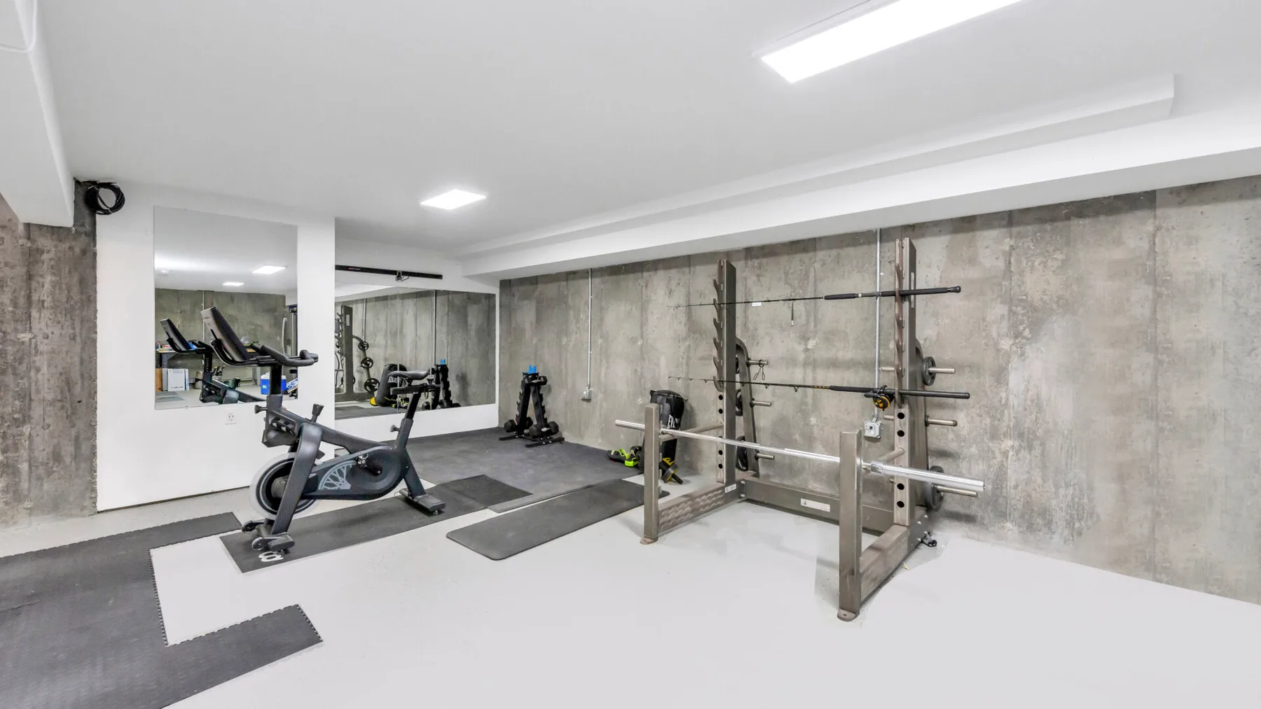 Un gimnasio con máquinas de ejercicio y un soporte de pesas junto a paredes de concreto.