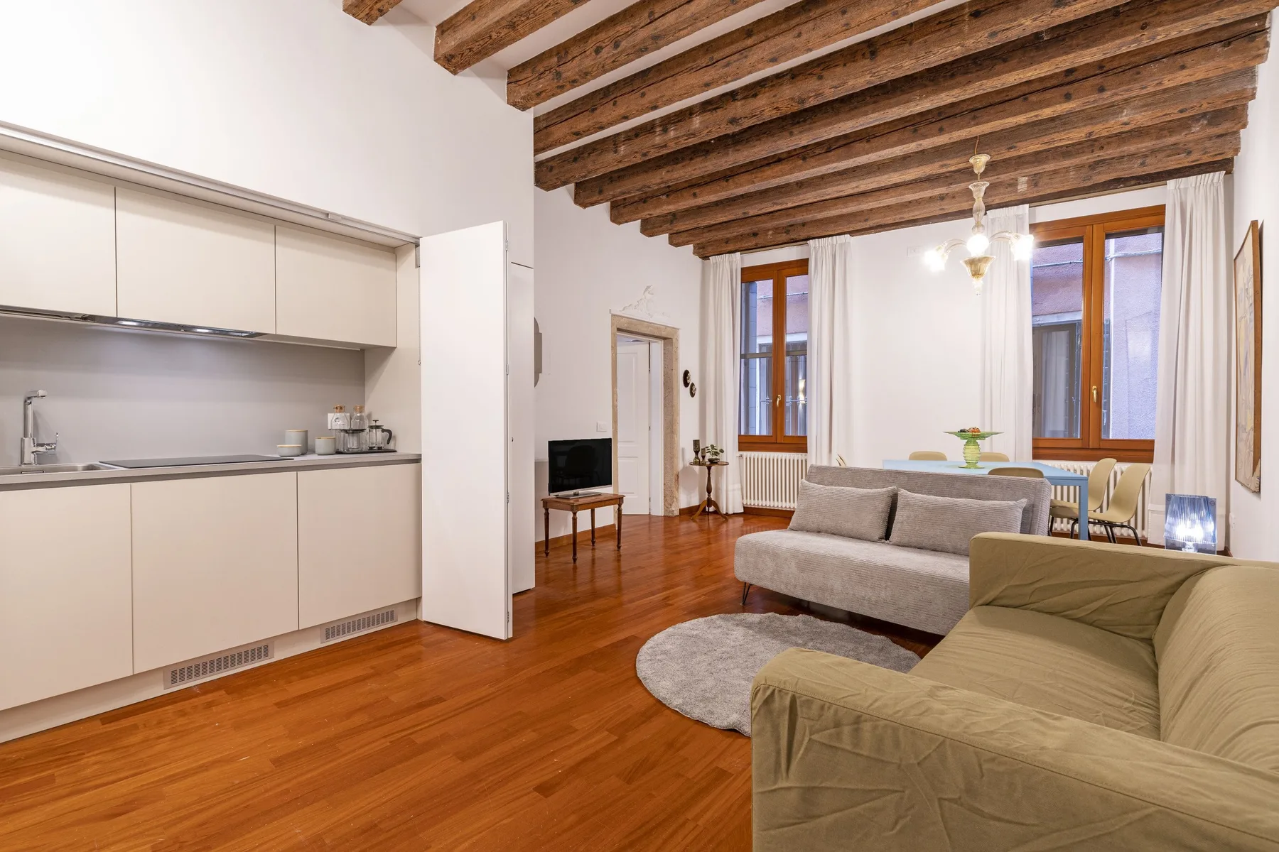 Una sala de estar con cocina abierta, techo con vigas de madera y asientos.