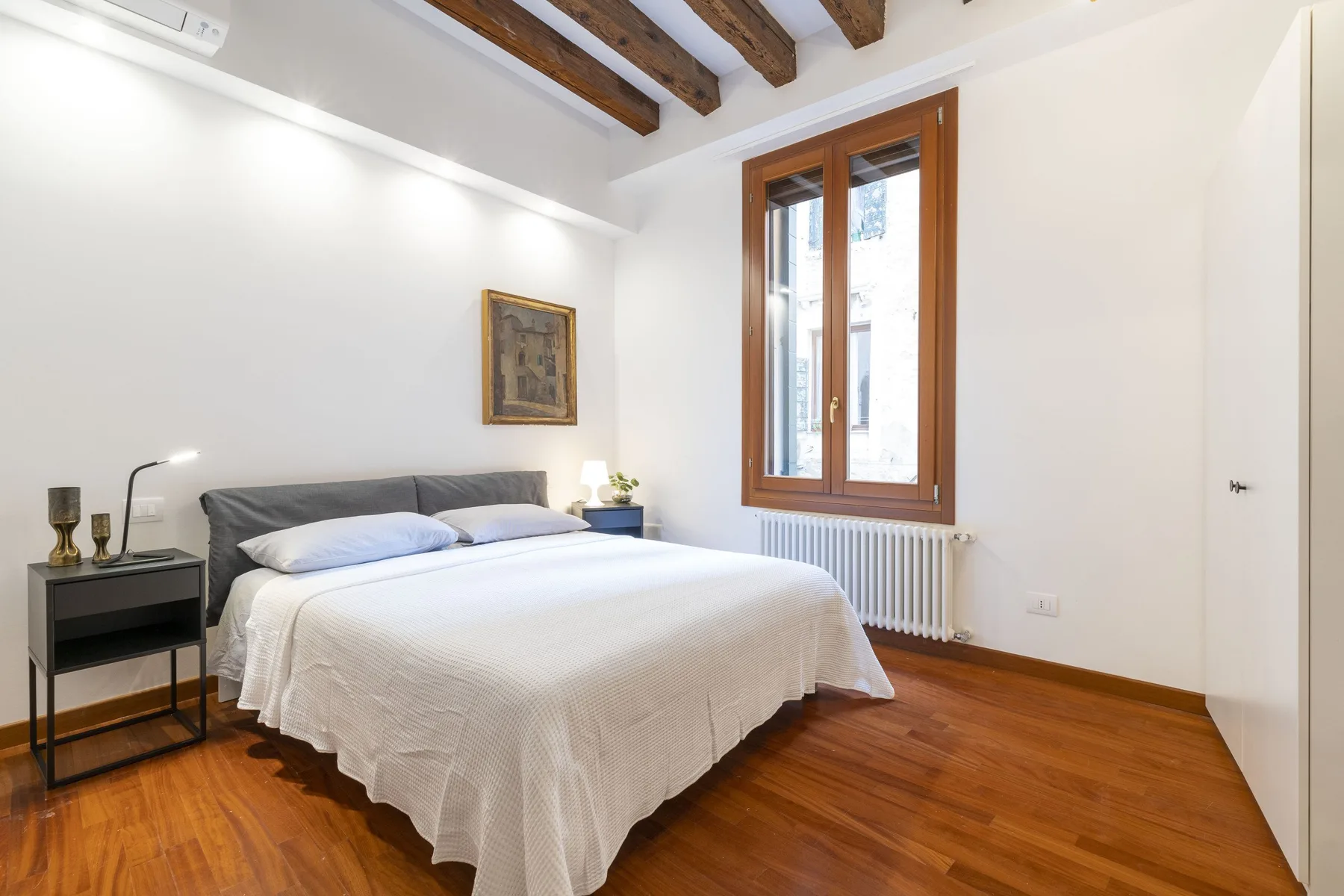 Un dormitorio luminoso con una cama bien tendida bajo vigas expuestas.