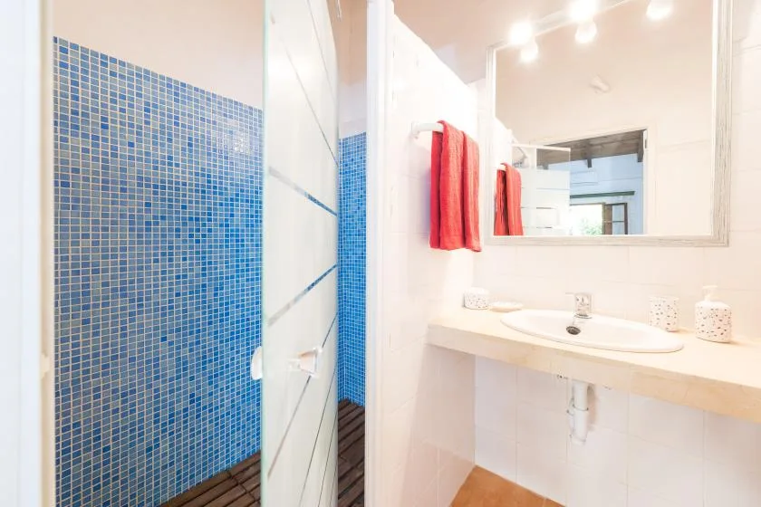 Un baño luminoso con lavabo, espejo y zona de ducha con azulejos azules.