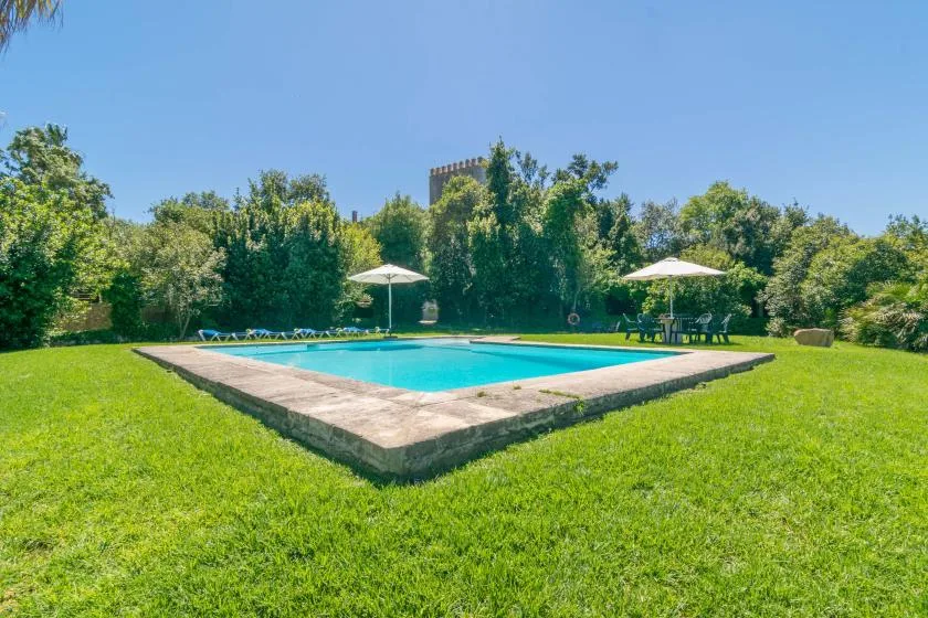 Una piscina al aire libre está en un jardín con césped, árboles y sombrillas.