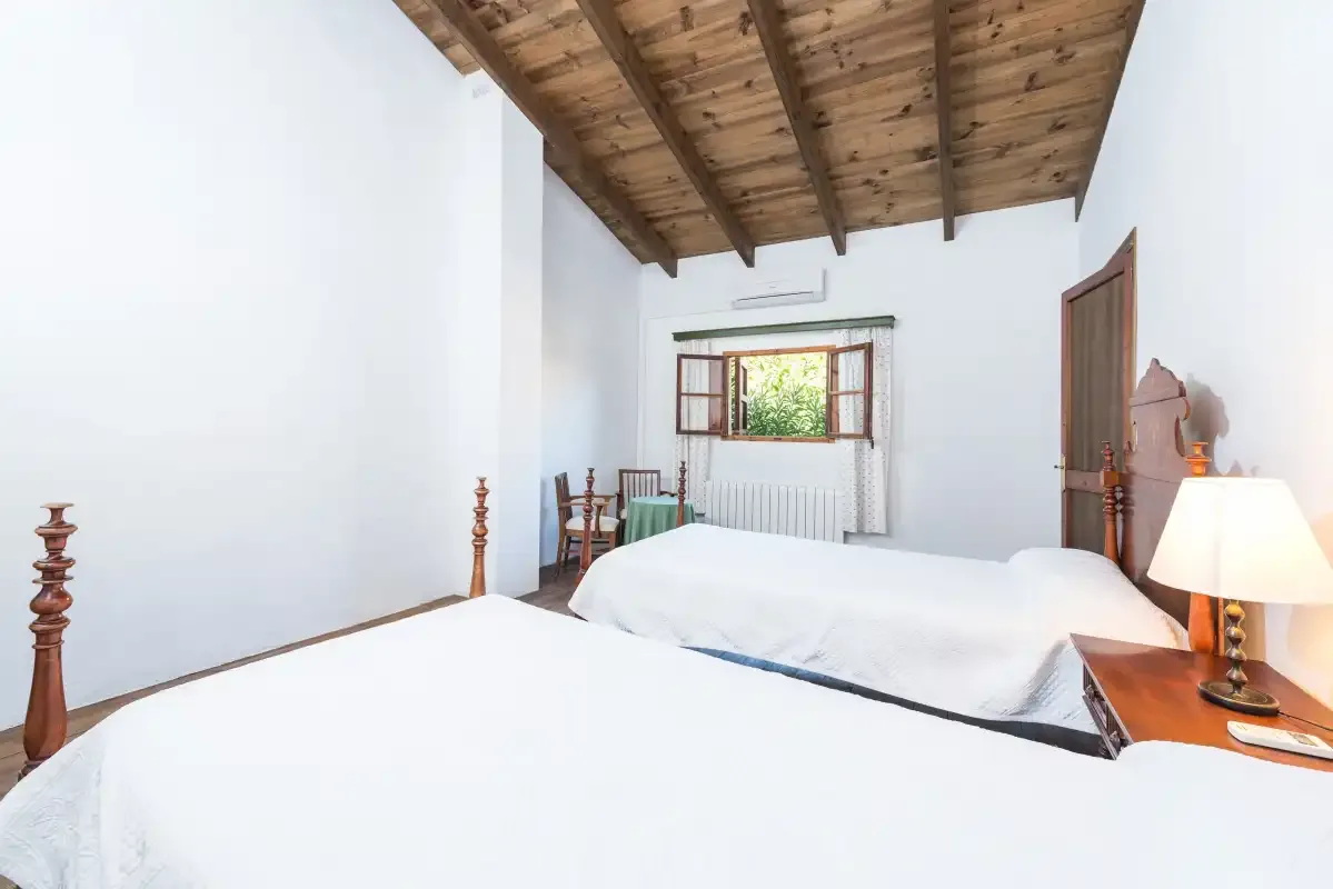 Un dormitorio con ropa de cama blanca, techo de madera y una ventana pequeña.