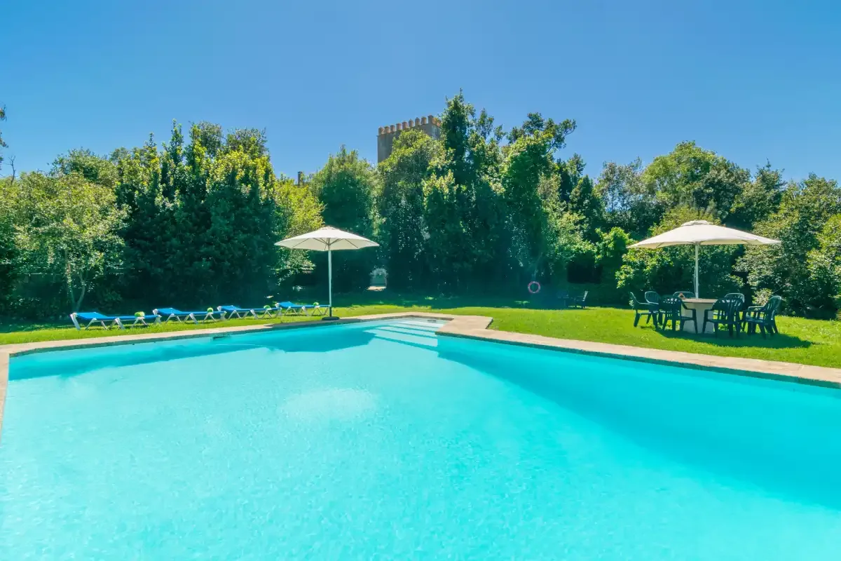 Una piscina al aire libre está rodeada de césped verde y árboles.