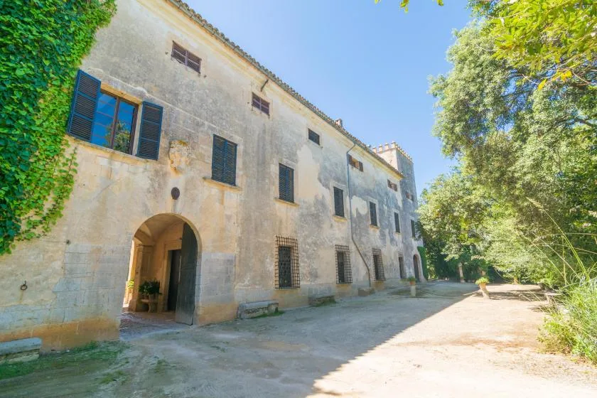 Un edificio de piedra con una entrada arqueada está junto a un camino arbolado.