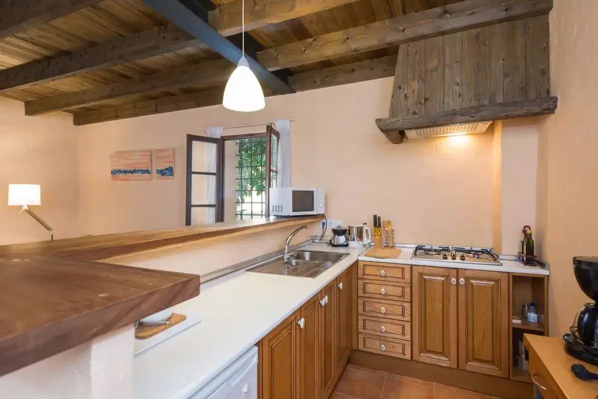 Una cocina rústica con armarios de madera y una encimera bajo vigas expuestas.