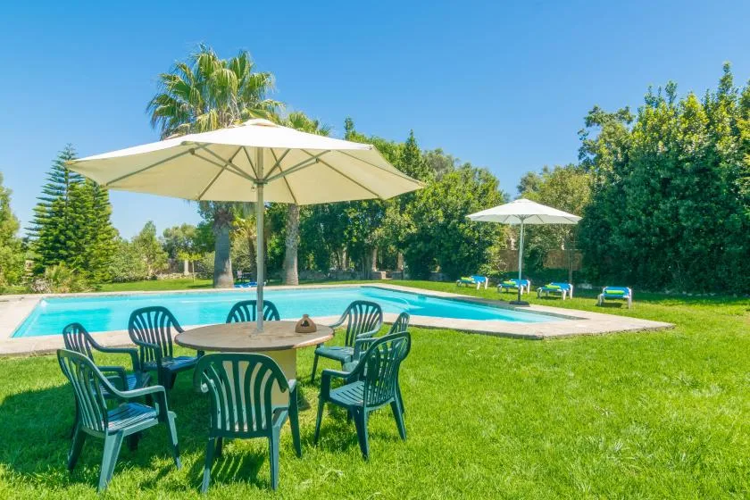 Una piscina al aire libre junto al césped, con asientos a la sombra de sombrillas.