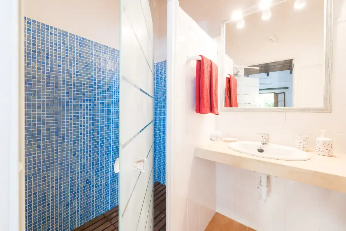 Un baño luminoso con un lavabo blanco y una ducha con azulejos azules.