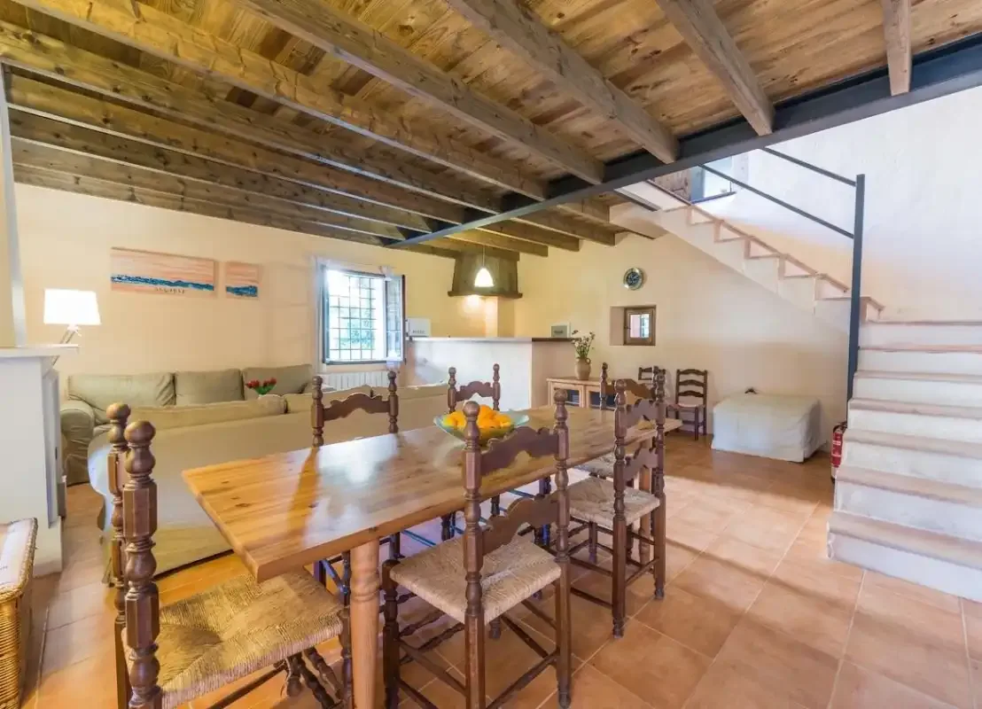 Zona de comedor y estar con una mesa de madera bajo vigas de techo vistas.
