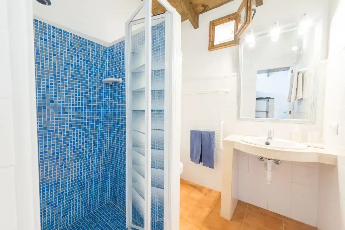 Un baño luminoso con una ducha de azulejos azules y un lavabo.