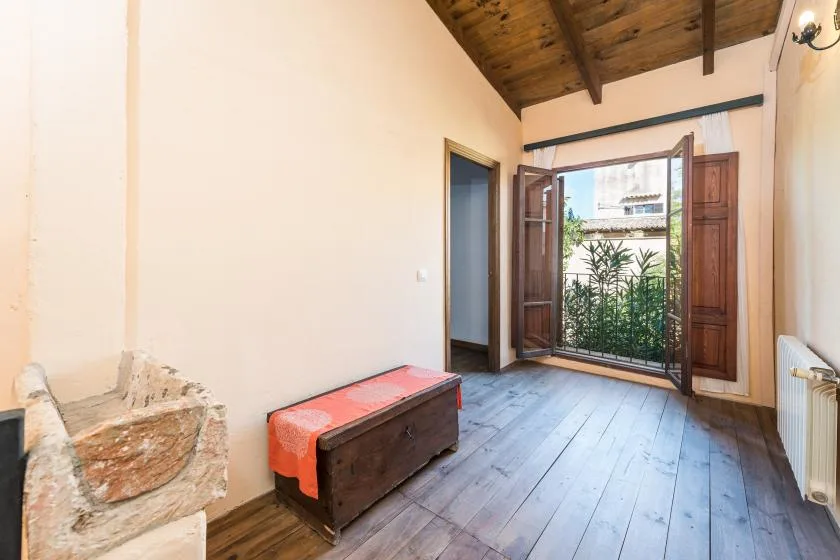 Una habitación luminosa con suelo de madera y puertas abiertas que dan a un balcón.