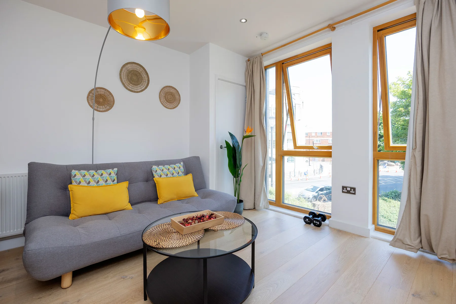 A bright living room with gray seating and tall windows.