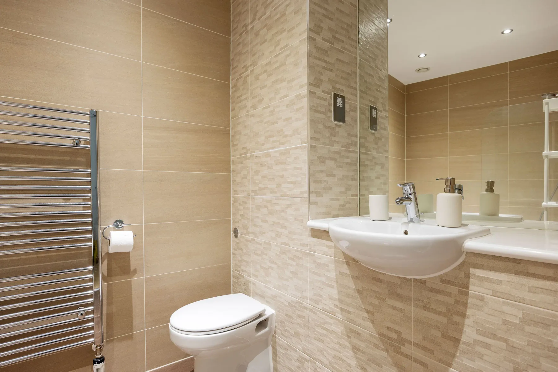 A tiled bathroom with a toilet, sink, and chrome towel warmer.