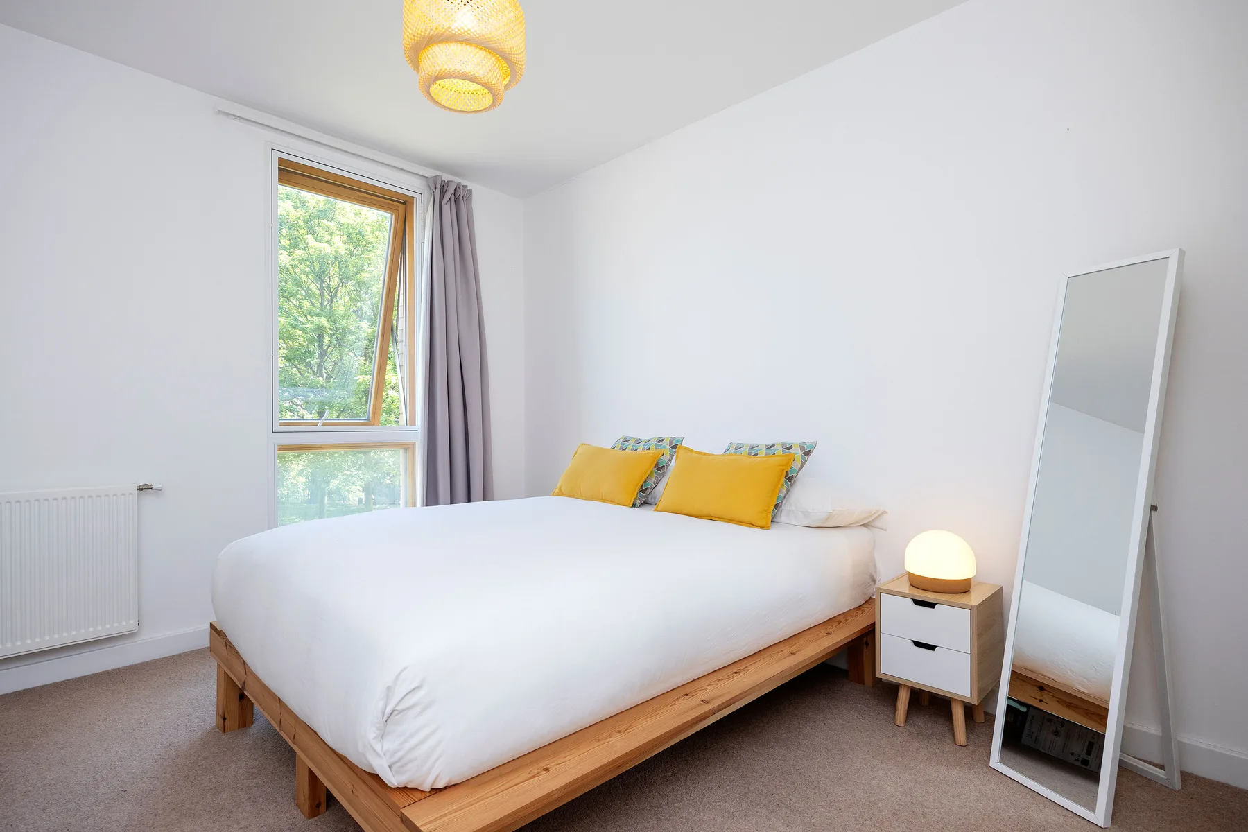A bright bedroom with a wooden bed, colorful pillows, and a large window.