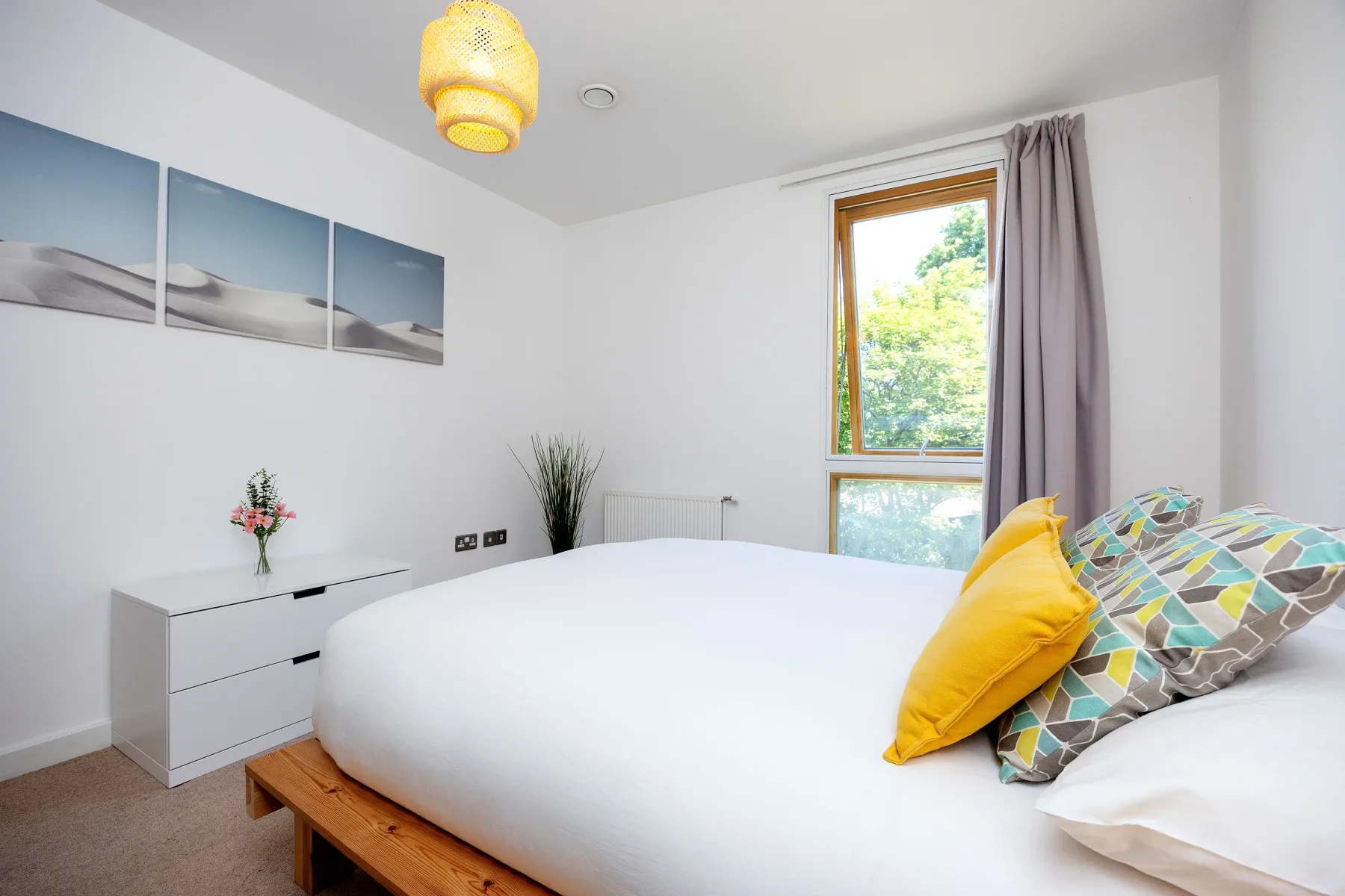 A bright bedroom with white bedding, colorful pillows, and a large window.
