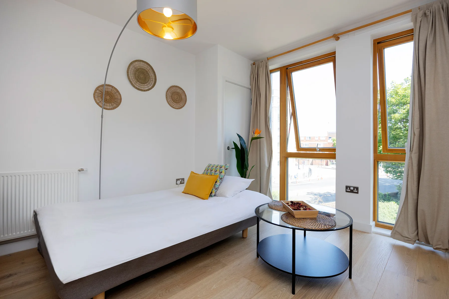 A bright bedroom with a bed, a round coffee table, and tall windows.