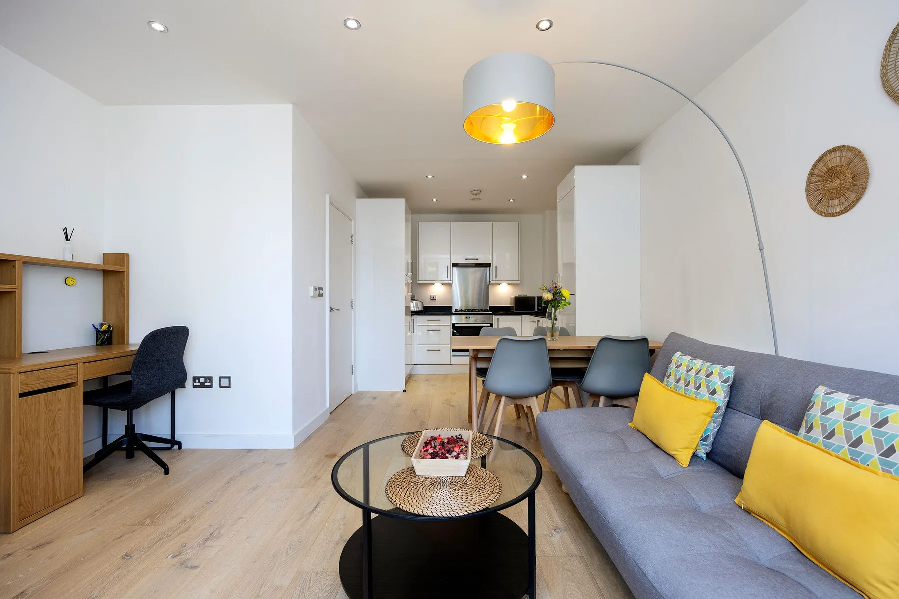 A bright living room with a gray sofa and an open kitchen in the background.