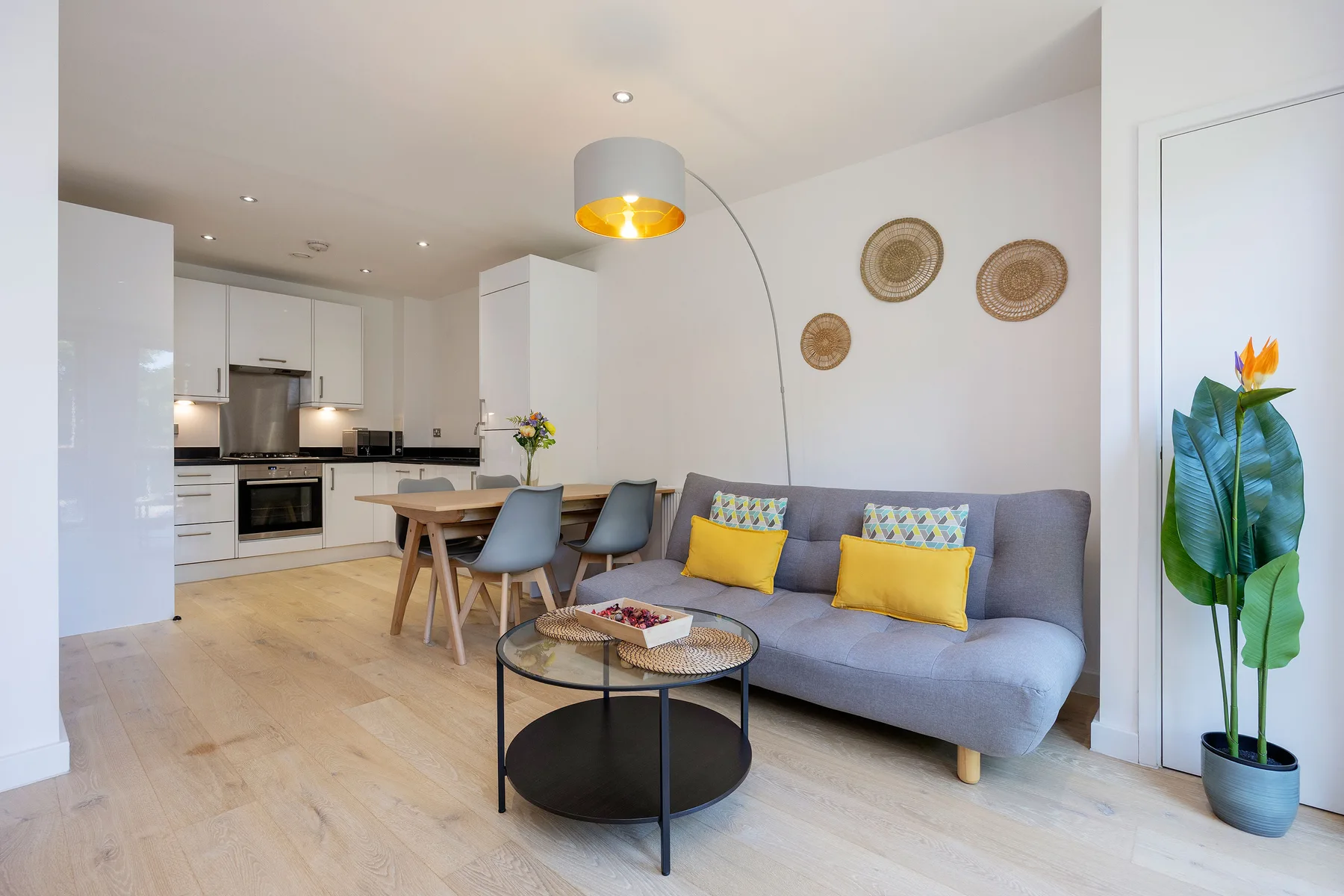 A bright living room with a gray sofa and an open kitchen.