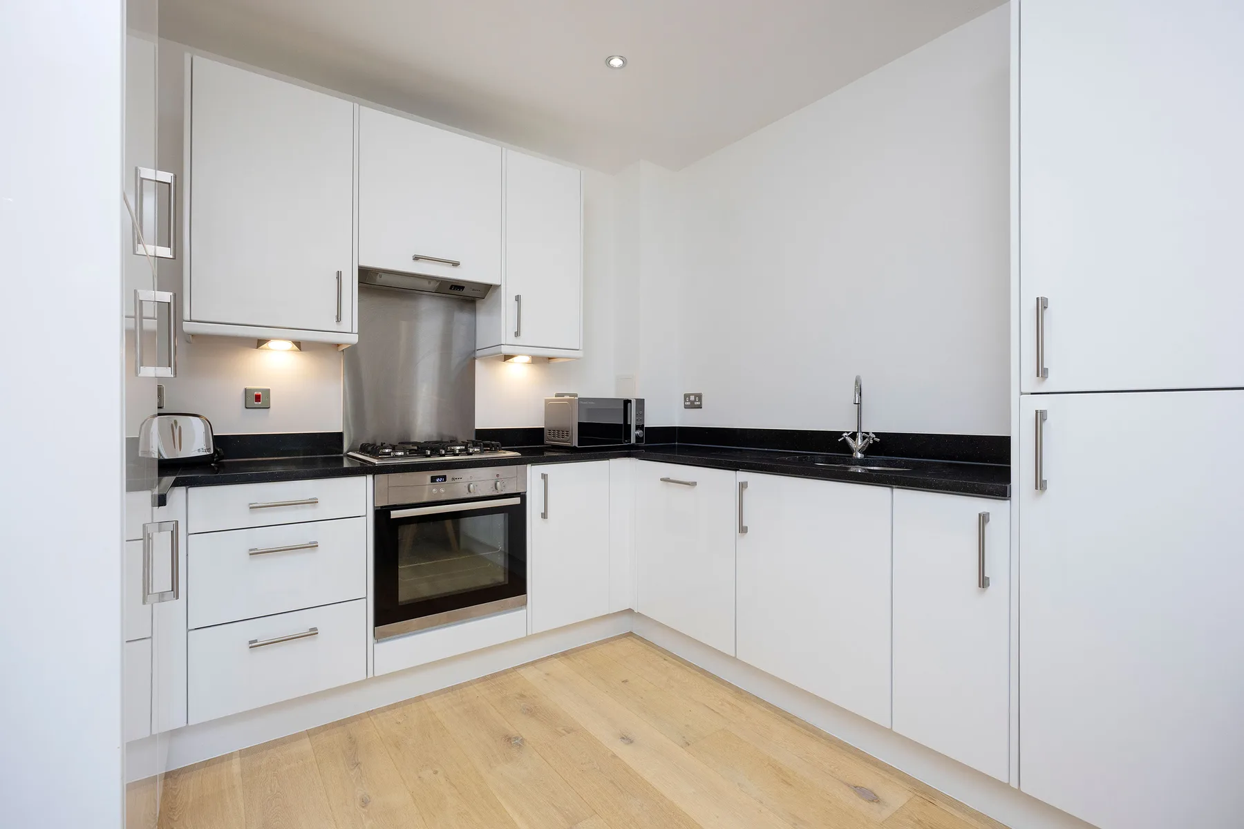 A bright kitchen with white cabinets, dark countertops, and an oven.