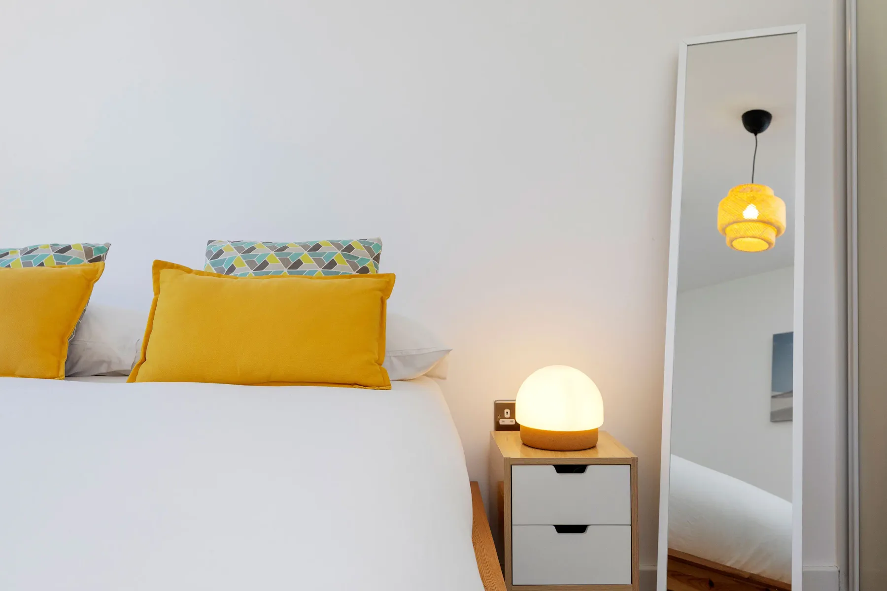 A bedroom with a bed dressed in white and yellow pillows beside a bedside table.