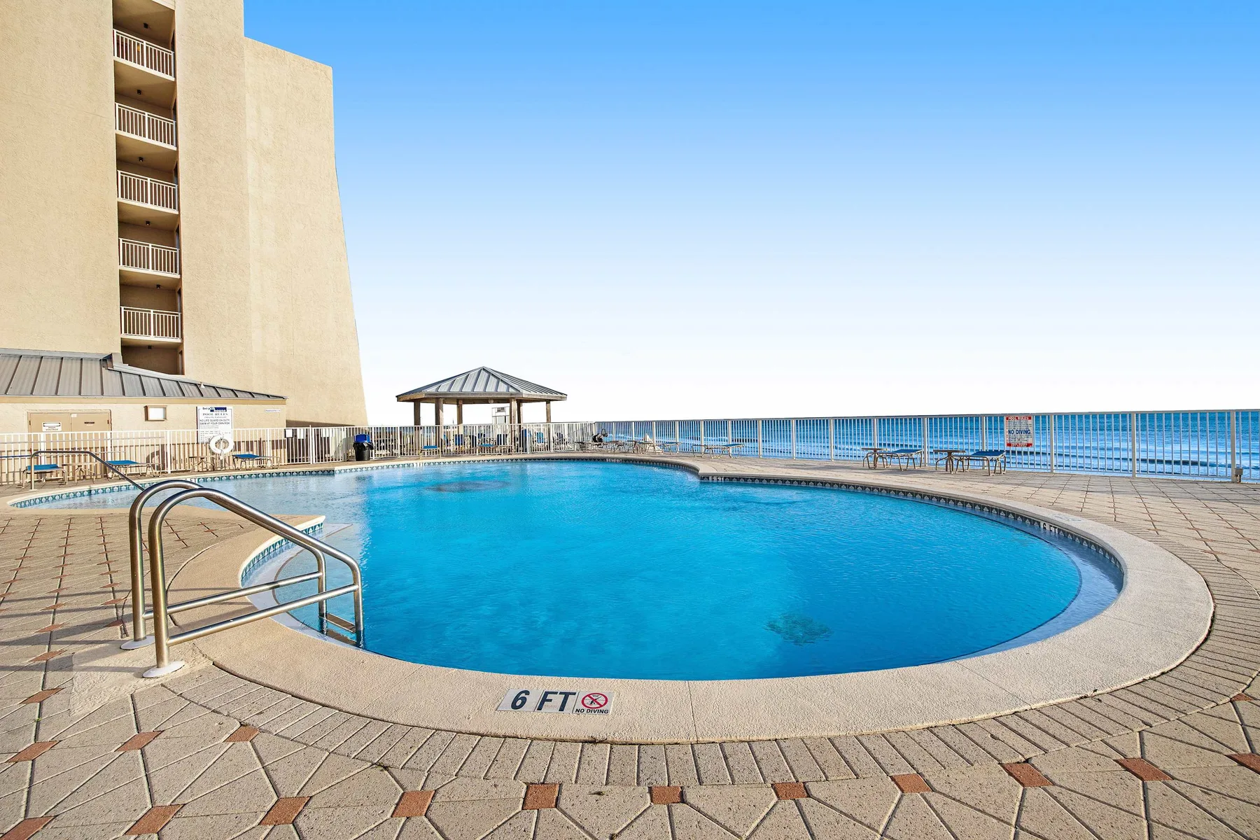 Una piscina exterior curva mira al océano junto a una terraza de baldosas.