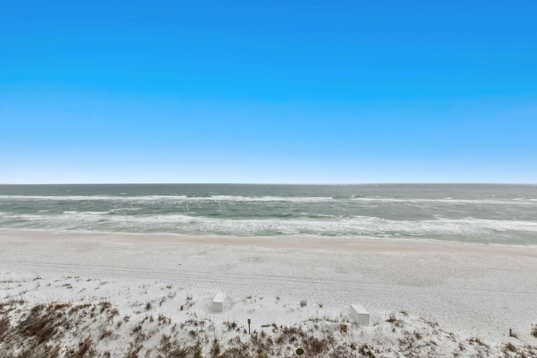 A sandy beach stretches along the ocean beneath a clear blue sky.