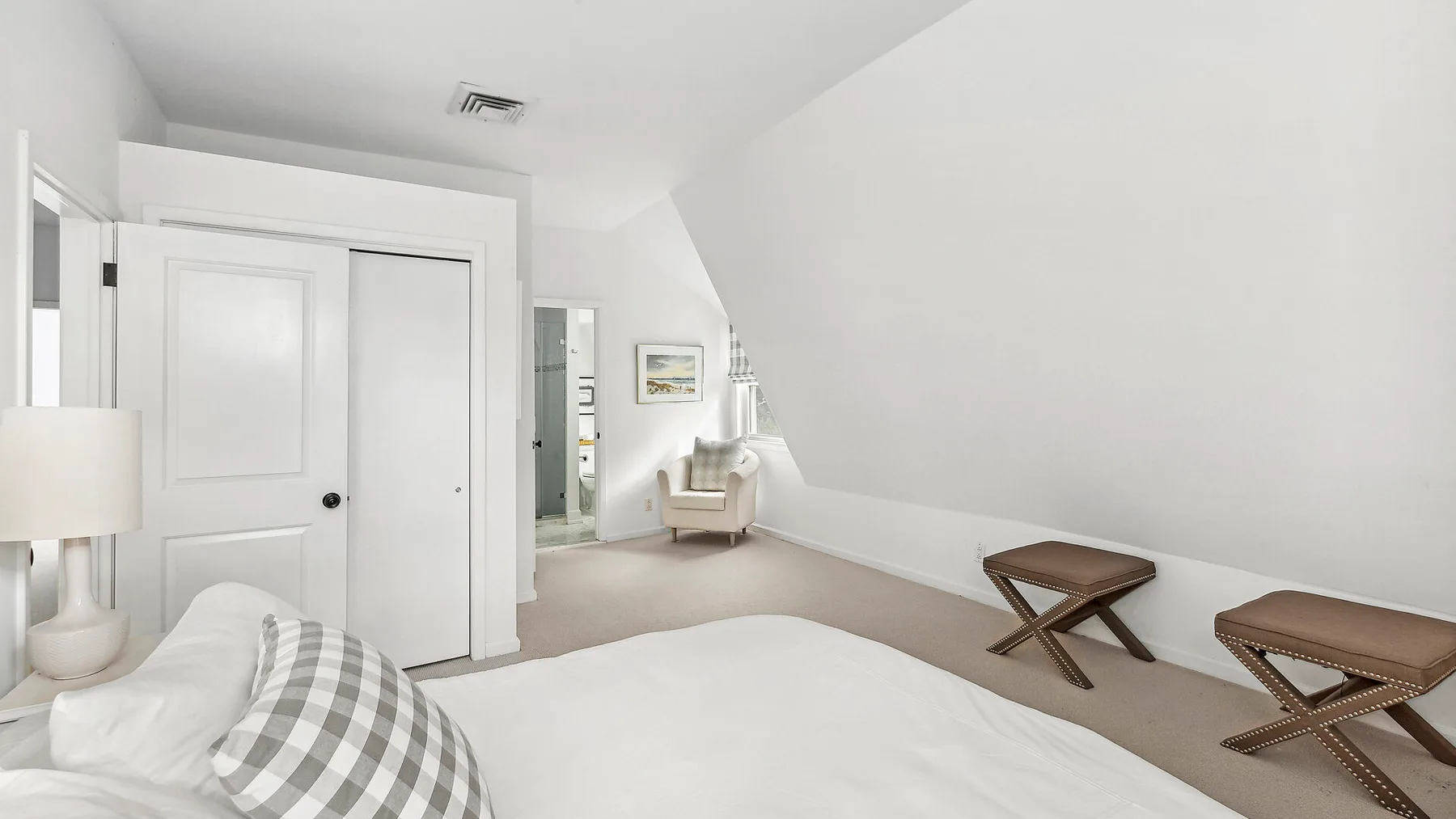 Un dormitorio luminoso con una cama, un sillón y dos mesas pequeñas.