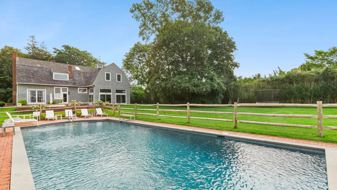 Una piscina junto a un césped y una casa grande.