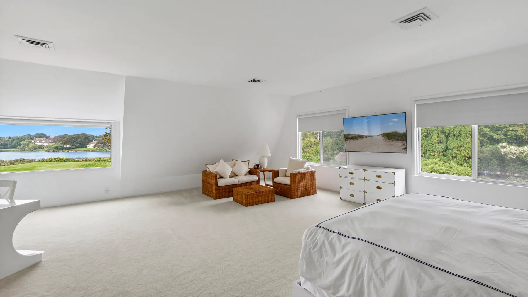 Un dormitorio luminoso con cama, zona de estar y amplias ventanas con vistas a la vegetación.