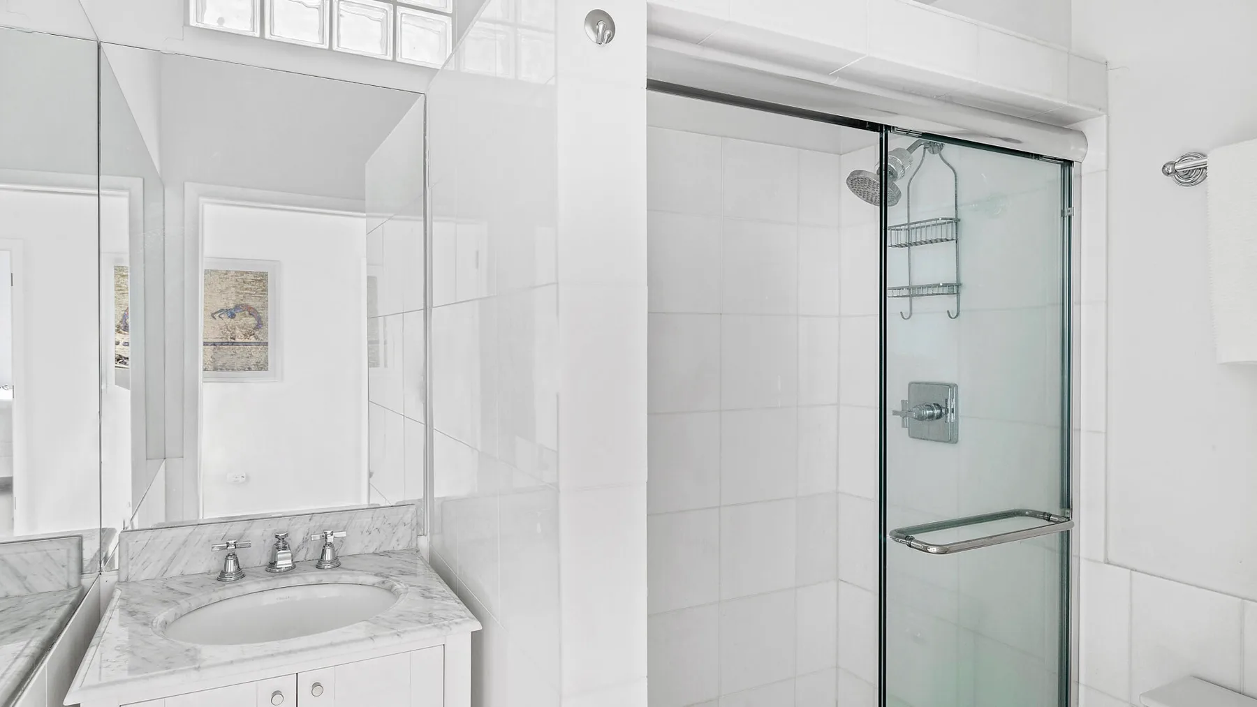 Un baño luminoso con azulejos, lavabo y ducha de vidrio.