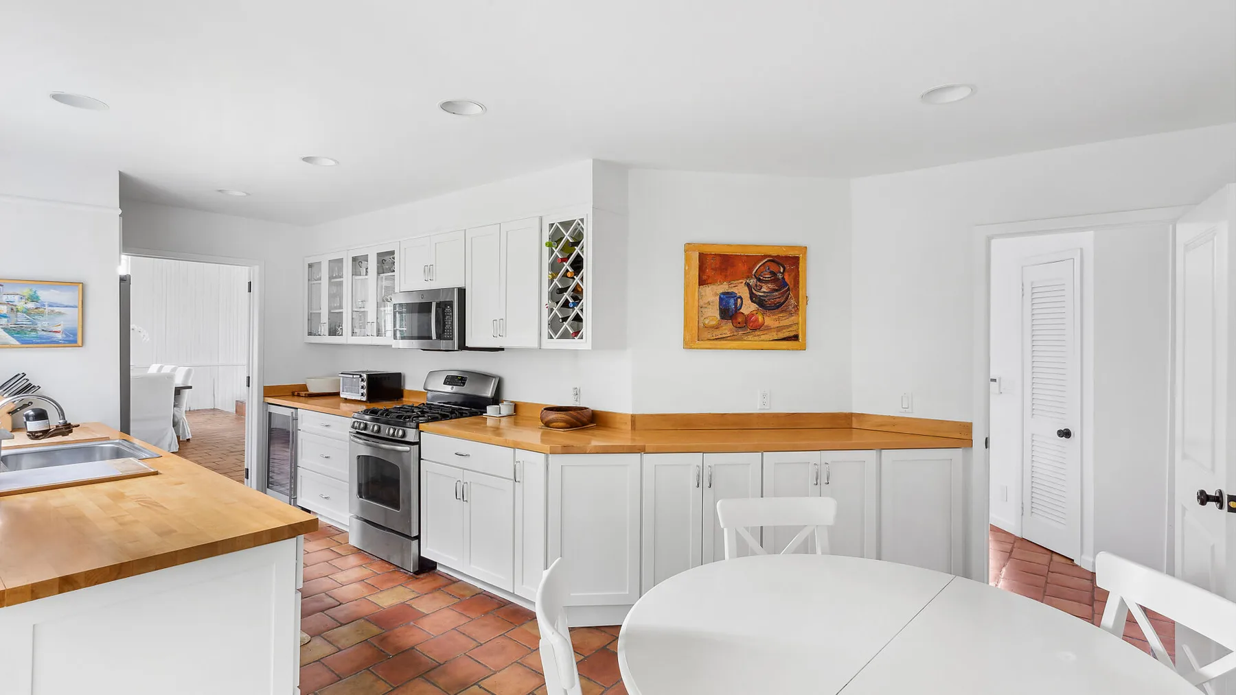 Una cocina luminosa con gabinetes blancos, encimeras de madera y una mesa redonda.