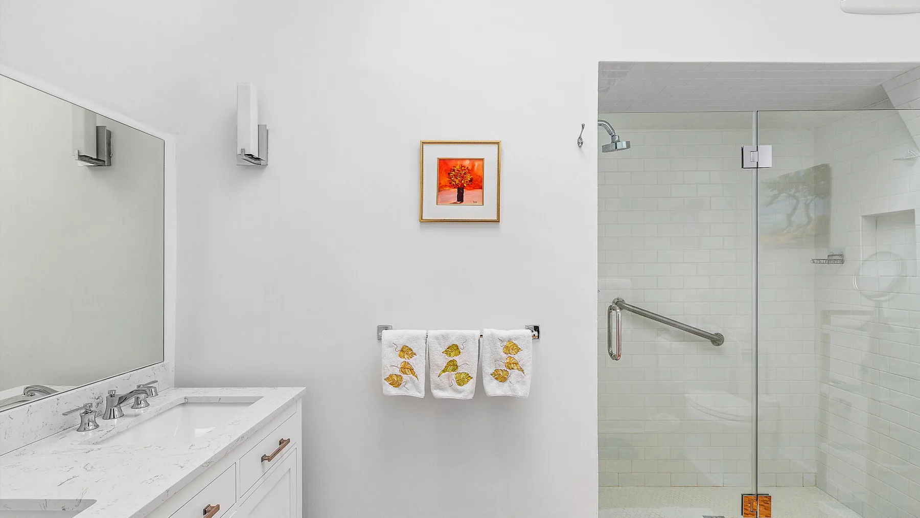 Un baño luminoso con lavabo, espejo de pared y ducha de vidrio.