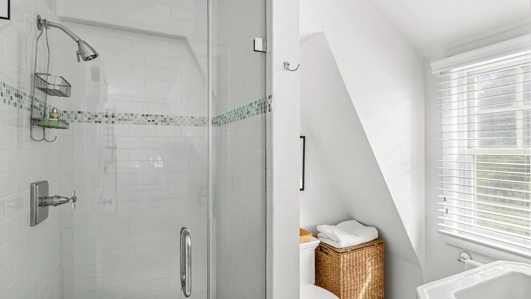 Un baño luminoso con una ducha de vidrio y una ventana con persianas.