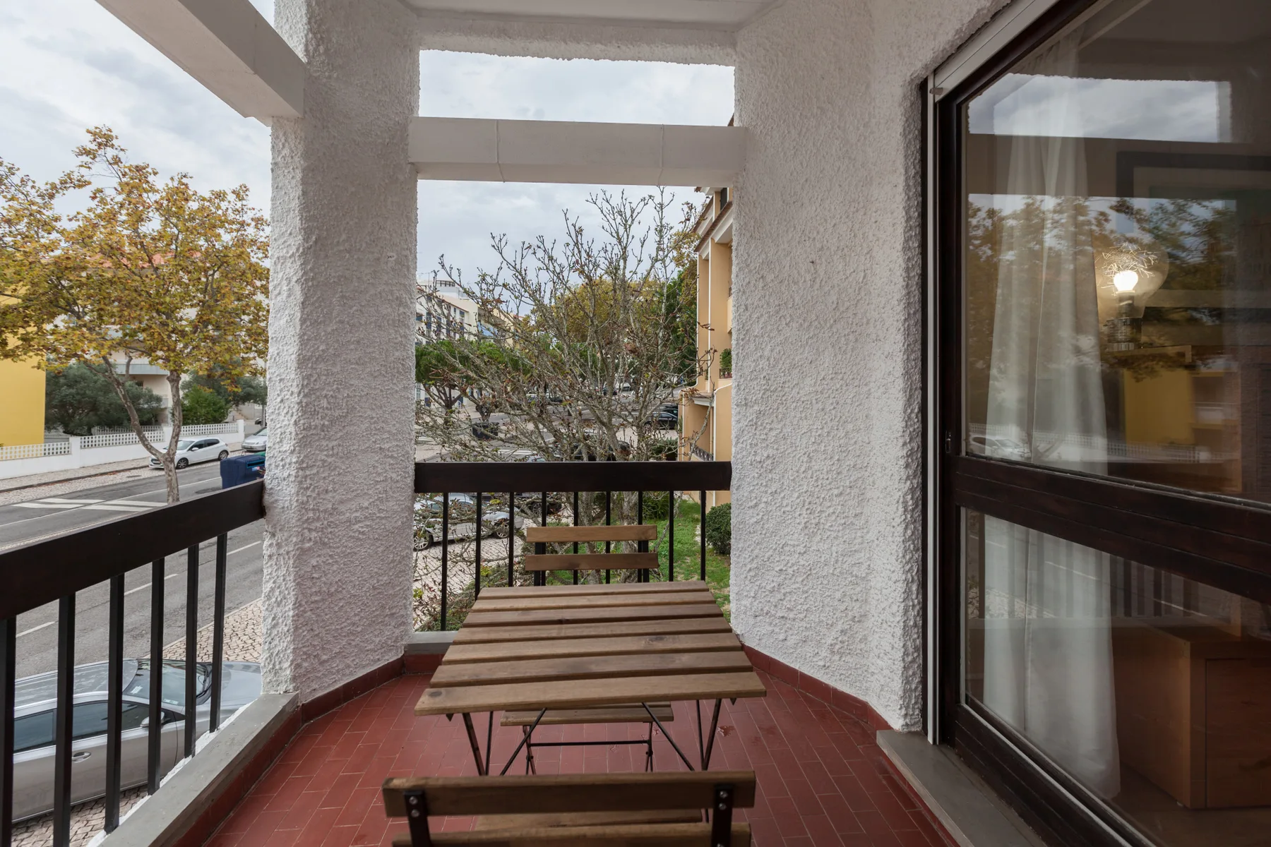 A covered balcony with a wooden table and benches overlooks the street.