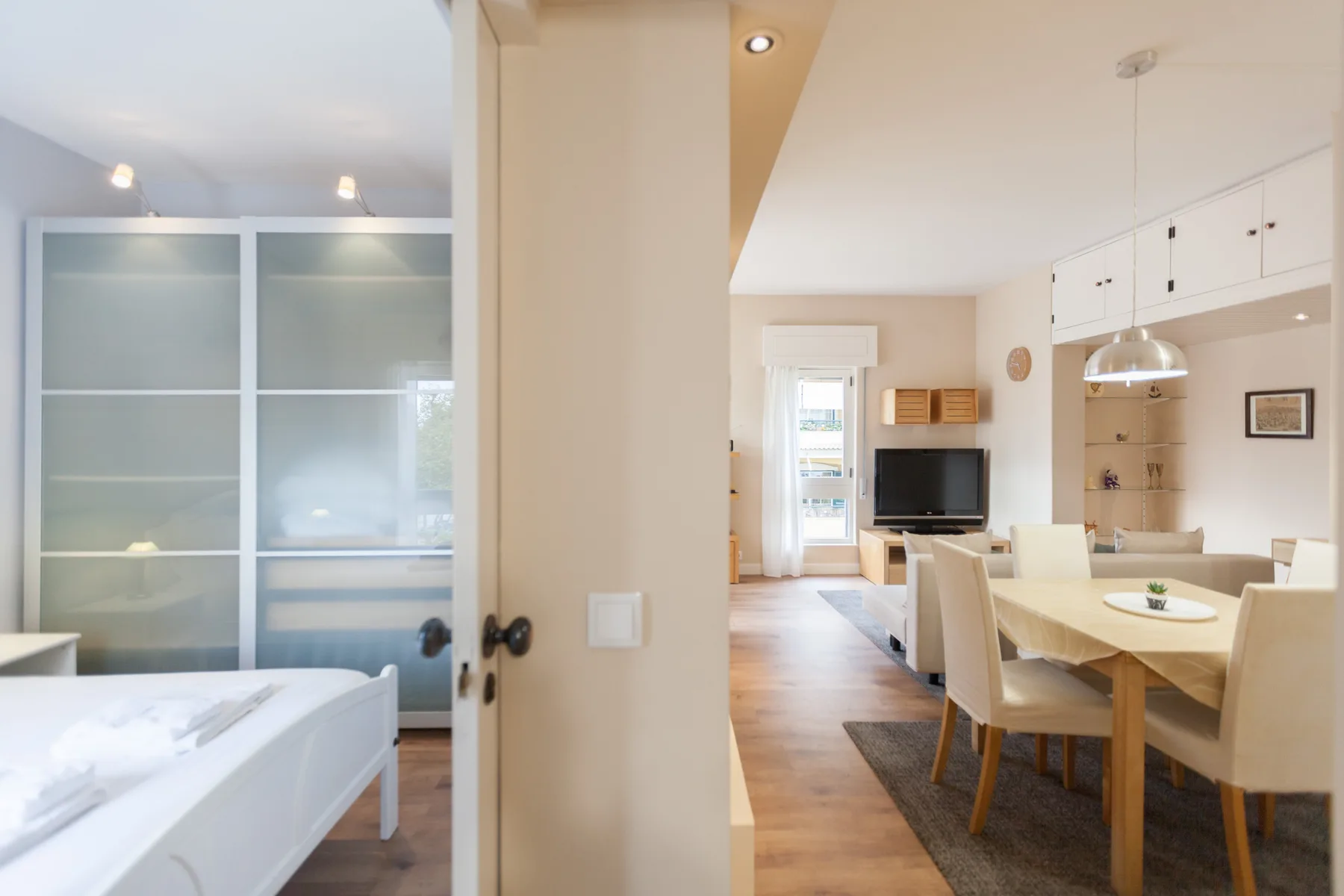 A bedroom opens onto a dining area with a table, chairs, and television.
