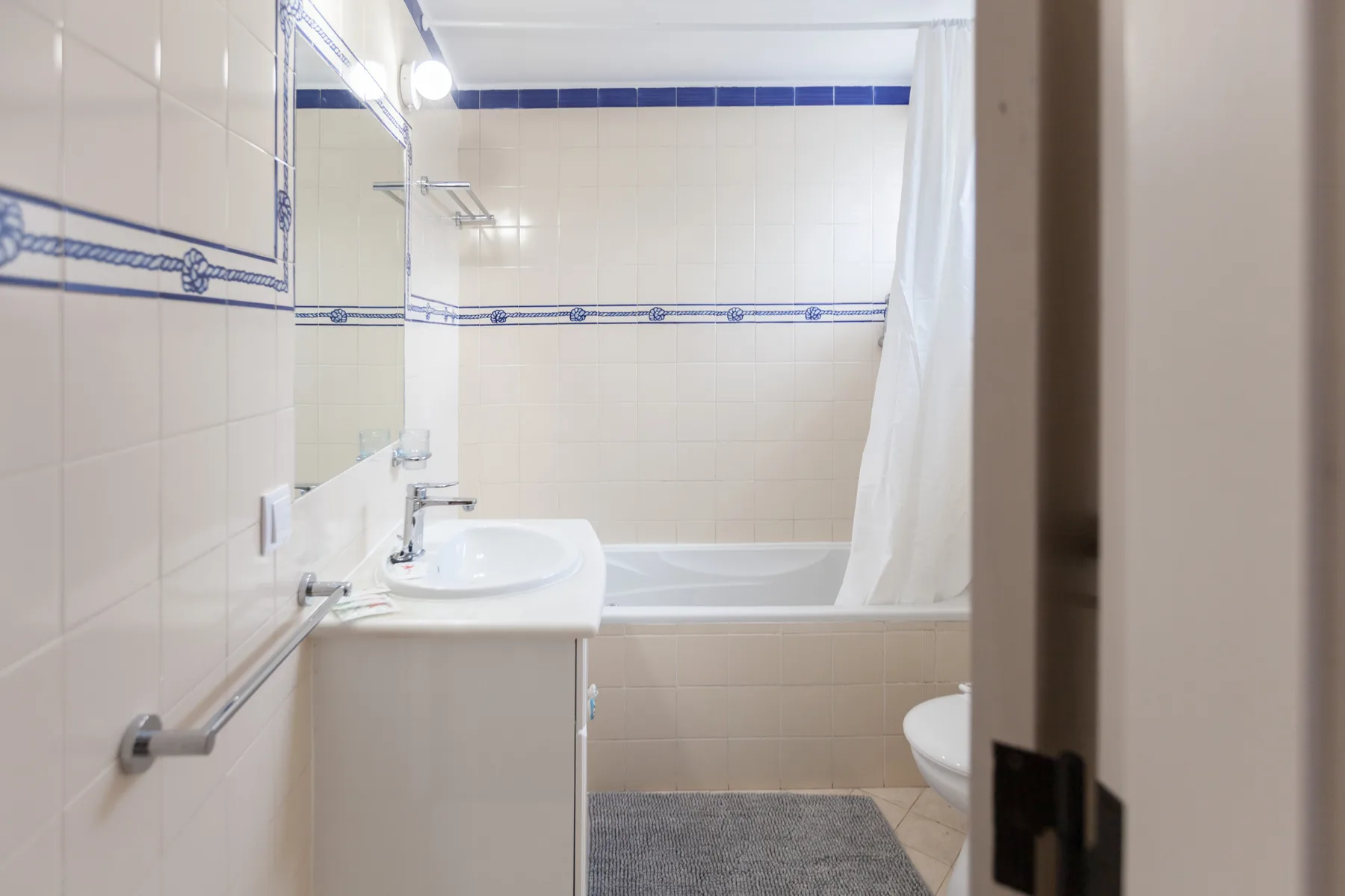 A tiled bathroom with a sink, bathtub, and shower curtain.