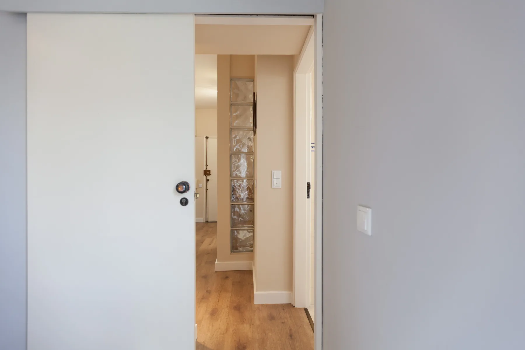 An interior hallway with light wood flooring and a narrow glass-block partition.