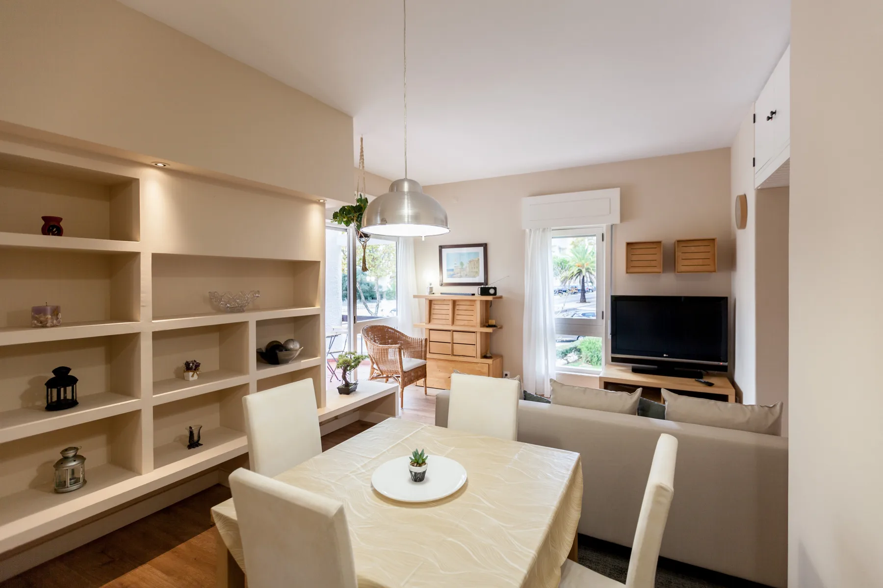 A bright living and dining area with a television and shelving.