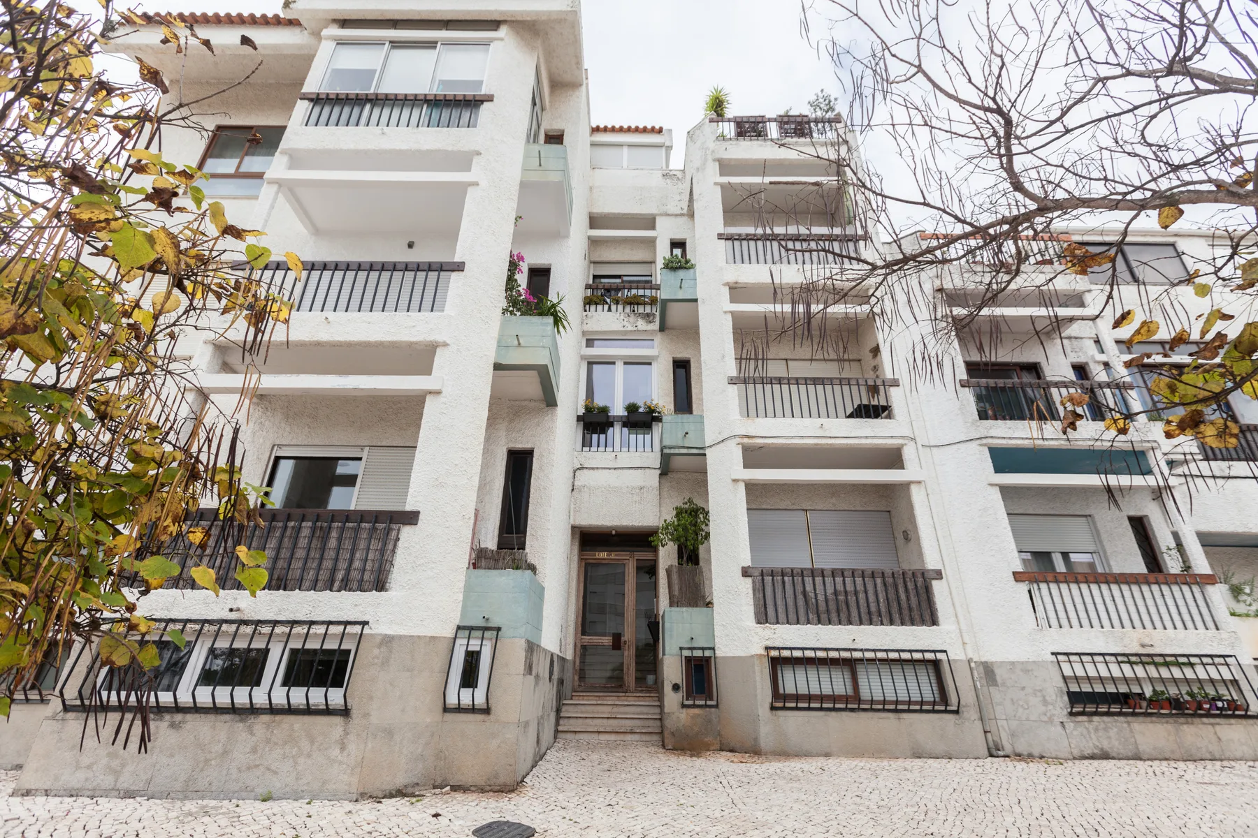 White apartment building with balconies facing a paved street.