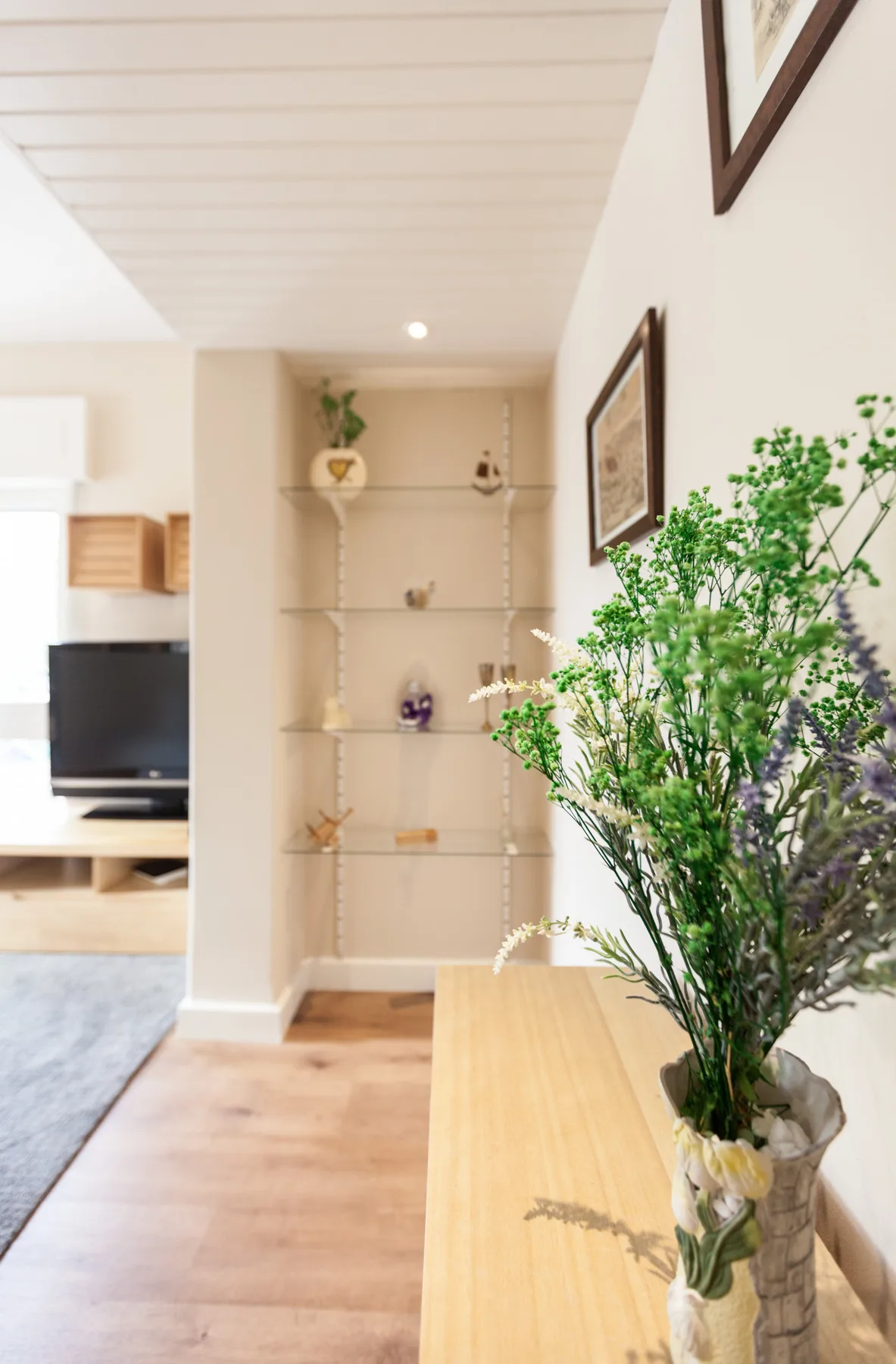A bright living room with open shelving and flowers arranged on a console.