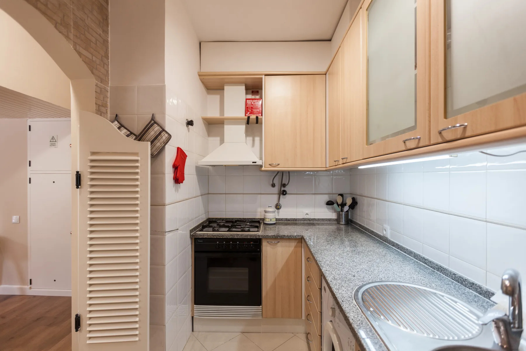 A compact kitchen with wood cabinets, a cooktop, and a sink.