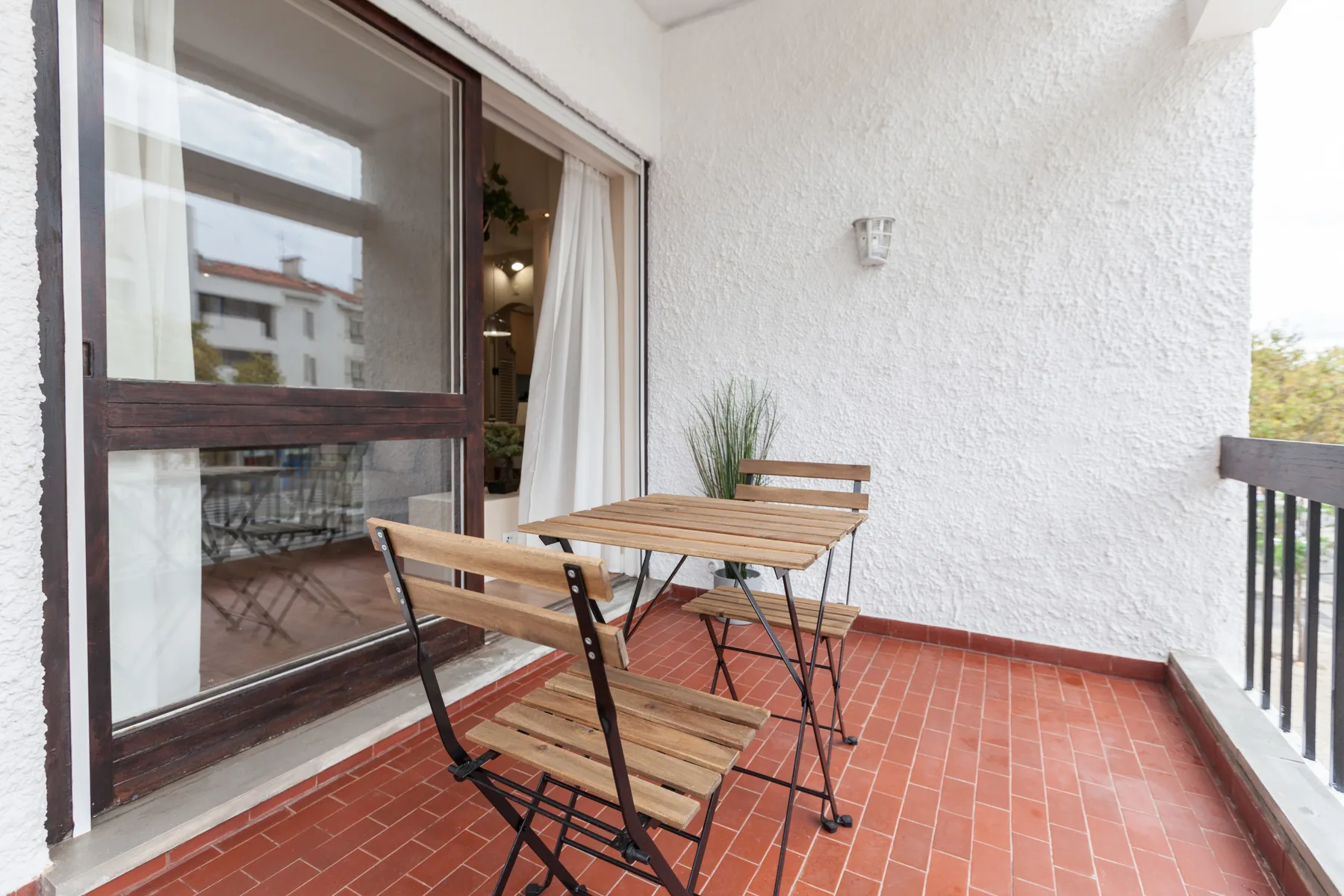 A small outdoor terrace with a wooden table and seating beside a glass door.