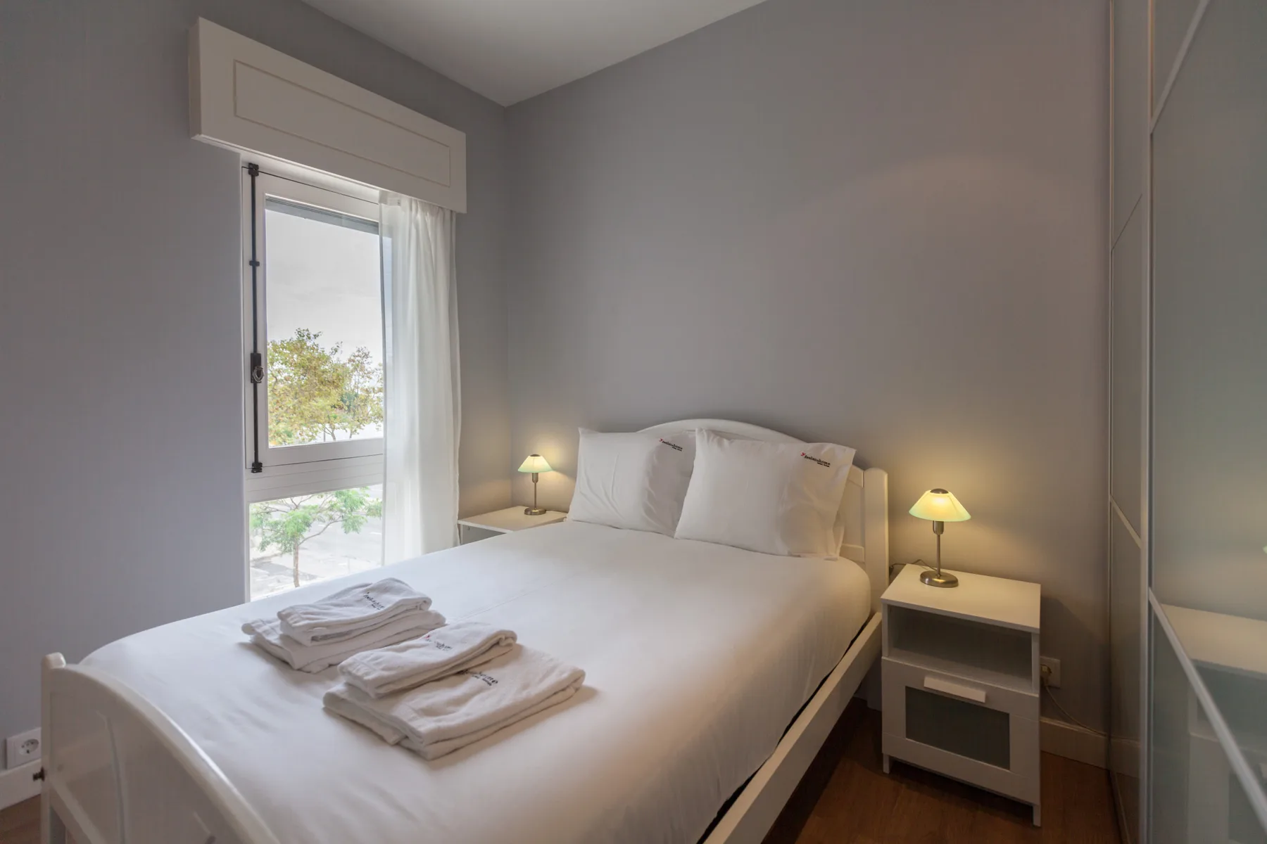 A bedroom with a neatly made bed beside a tall window.