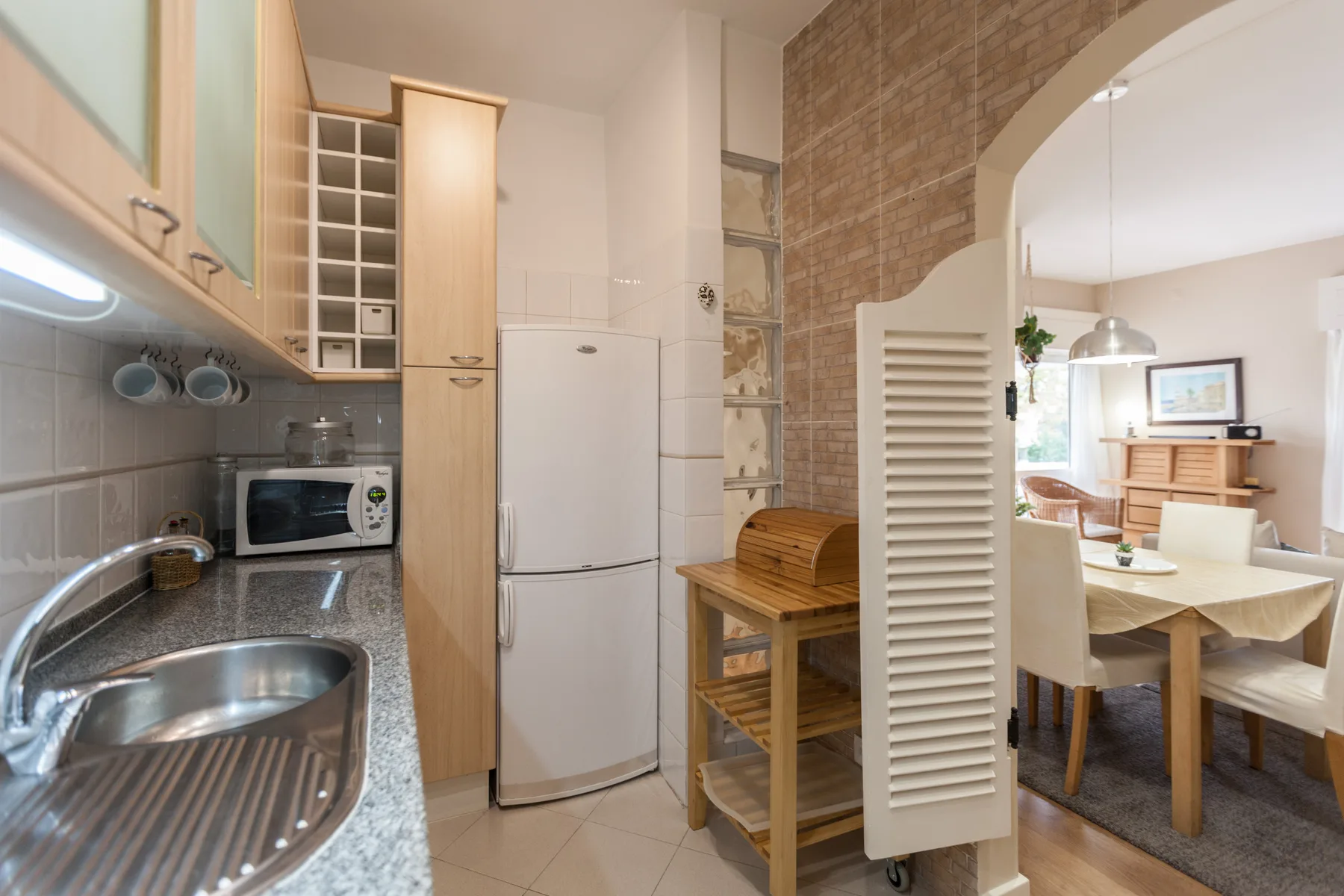 A kitchen with a refrigerator and countertop opens into a dining area.