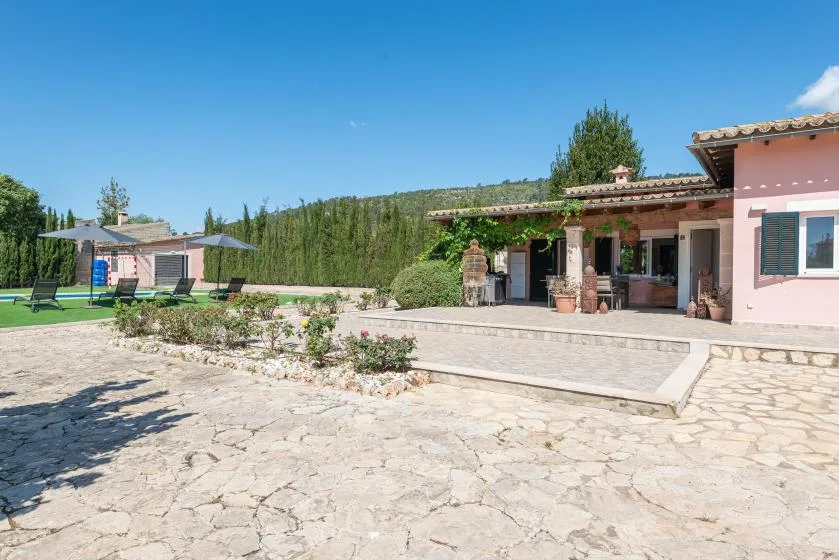 A stone patio beside a pink house overlooks a lawn and swimming pool.