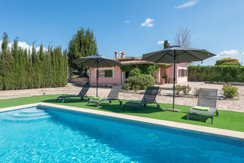 An outdoor swimming pool beside a pink house, with loungers on the lawn.