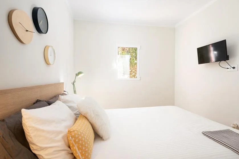 A bright bedroom with a bed, wall-mounted television, and small window.