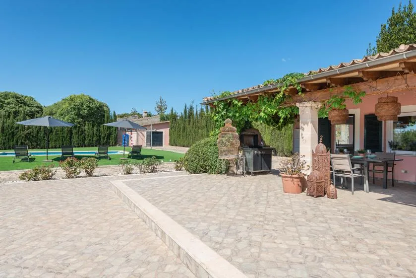 Un patio pavimentado junto a una zona de comedor exterior con sombra y un jardín.