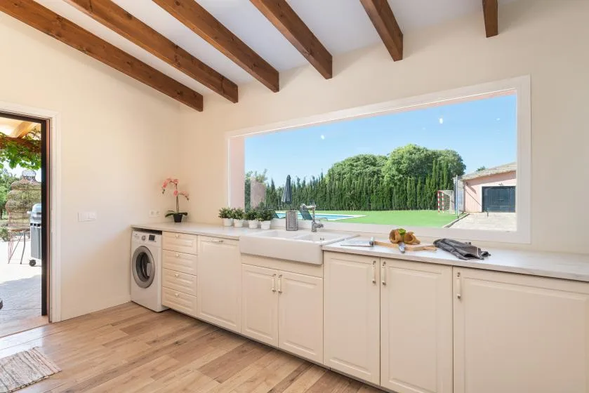 A bright kitchen with a long counter beneath a wide window overlooking the garden.